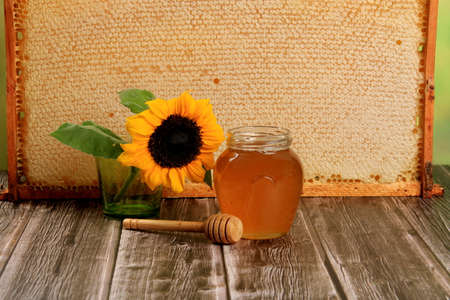 Honeycomb in a wooden frame decorated with sunflower and glass jar of honey on a wooden background. Beekeeping conceptの写真素材