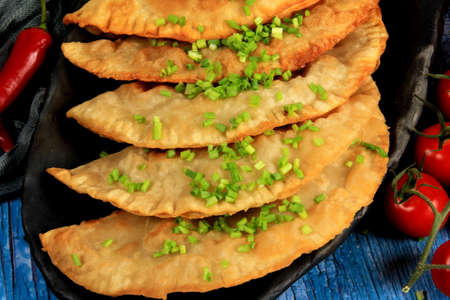 Hot homemade chebureki pies with minced meat, onion and pepper on plate, wooden backgroundの写真素材