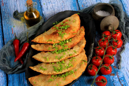 Hot homemade chebureki pies with minced meat, onion and pepper on plate, wooden backgroundの写真素材