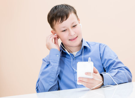The boy listens to music at the table