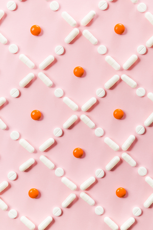 Pattern of white and orange pills and tablets on a pink background.の写真素材