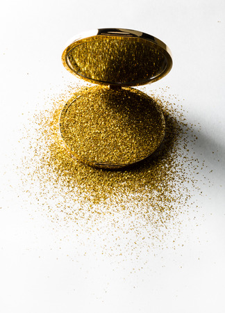 Powder highlighter in a gold powder box with gold sparkles reflected in the mirror. Isolated on white background.の写真素材