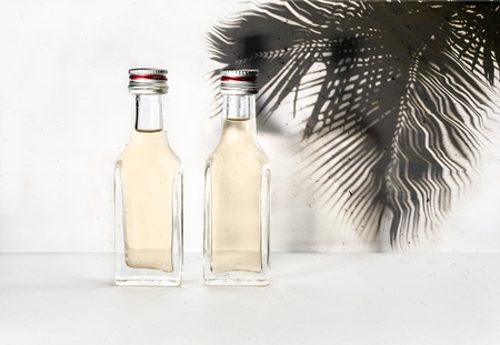Two bottles with an alcoholic drink on a background with the shadow of a palm leaf.の写真素材