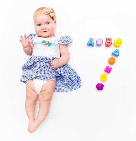Portrait of a sweet infant baby girl wearing a pink dress and headband bow, isolated on white in studio with number seven from toysの写真素材