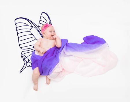 Laughing baby girl wrapped in fabric on cloud with painted butterfly wingsの写真素材