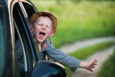 Child boy sticking his head out of a car window. Kid sitting in safety seat and looking through window paneの写真素材