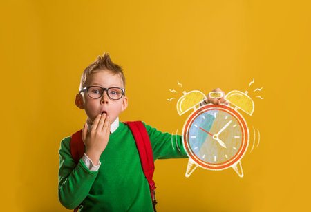 Smart kid in glasses with bag. Happy child against blackboard. Drawing alarm clock
