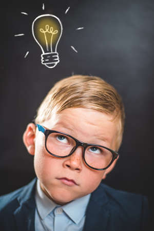 Thinking child with bulb at the blackboard. School concept. Genius. Go back to school. Little businessman with bright ideaの写真素材