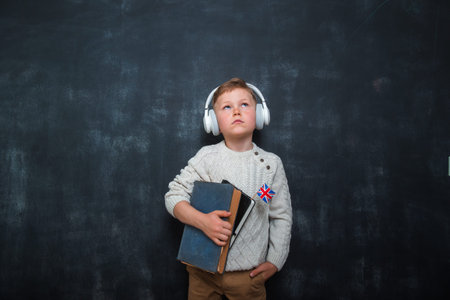 Kid in uniform and headphones holding a flag of United Kingdom and book in hands. Great Britain...