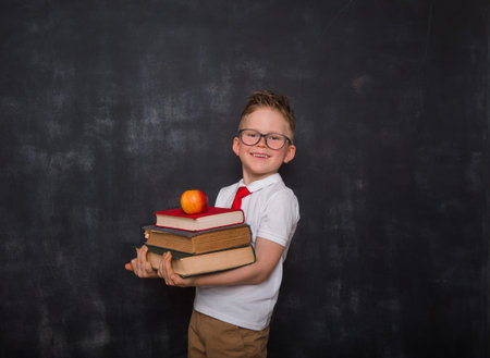 Adorable child whit books and apple in hands. Back to school. Education. Blackboard on background....