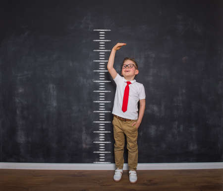 Little kid boy measuring himself. School boy measuring his growth in height against a blackboard scale. Back to school. Ready to go to school