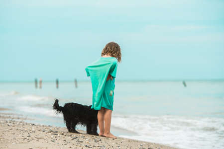 Child walking alone with dog at the beach. Back view. Kid in a big t-shirt with little blck dog. Beafoot on sand. Ocean. Best friend animal pet dogの写真素材