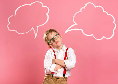 Schoolboy in glasses near blue wall with text cloud with space for your text. Thinking kid. Dream big. Back to school. Little businessmanの写真素材