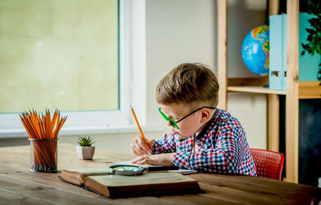 Little boy write on blank paper on desk near the window. Back to school. Educate at home and doing homeworkの写真素材