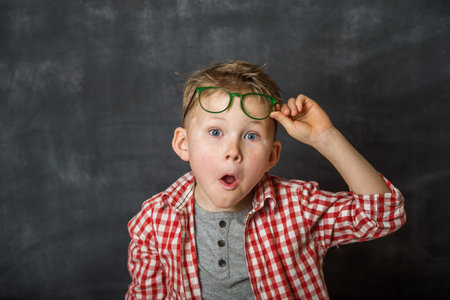 Kid boy portrait with funny shocked face expression. Kid with open eyes. Child is Picking up glasses aboveの写真素材