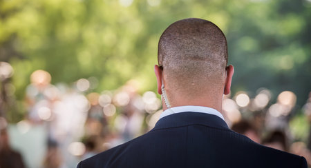 Security guard standing in the business meeting. Mature security guard listening to earpiece against crowd. Secret service agent listening to his earpiece, side. Bodyguardの写真素材