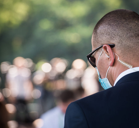 Protection and guard service. bodyguard man with earphone and black eyeglasses and business suit wearing a mask during the Covid outbreak, during a public visit of a dignitary.の写真素材