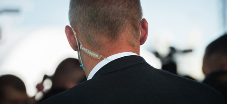 Security officer use radio.. bodyguard standing and listening message with security earpiece on helipad. Security guard man on event. Secret service. Private guard in suit standing in crowdの写真素材