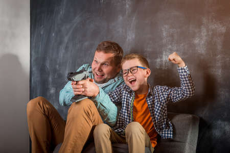 Dad and son. Funny family time hobby together at home. Little school child son playing with happy young father. Excited two male generations family enjoying video gameの写真素材
