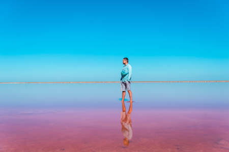 Man standing in pink water with blue sky above. pink salt lake. Exploring nature, travel, family vacation in Kherson region, Ukraine. Happy time for people to improve healthの写真素材