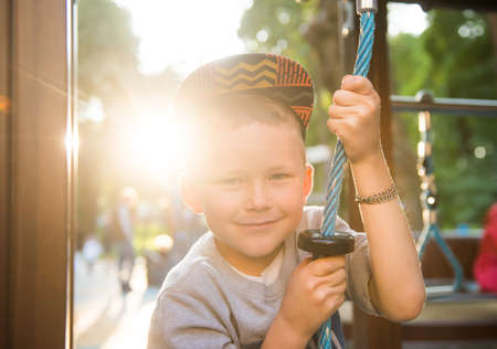 Funny smiling child playing outdoors. Little caucasian boy hanging on the monkey bar by his hand to exercise at outdoor playground. Kid boy in sunlightsの写真素材