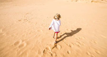 Little kid running and jumping in sand. The largest desert in Europe. Desert landscape with sand waves. Dunes background. Sandy dunes with footprints. Oleshky Sands in Kherson region, Ukraine.の写真素材