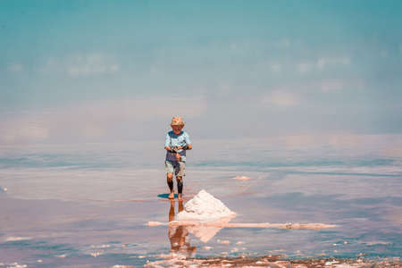 Funny little kid boy running in pink salt lake on a sunny. Exploring nature, travel, family vacation in Kherson region, Ukraine. Happy time for childの写真素材