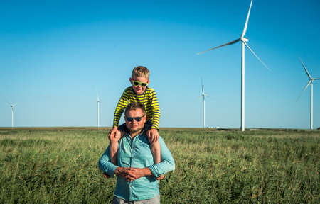 Wind turbine field. Father carrying son on shoulders and waving their arms like a windmill.の写真素材
