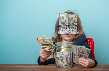Education for kids how to be rich. Child with dollar bills shoved over glasses covering eyes. Financial independence and ability to earn a lot of money. Back to school.の写真素材