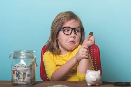 Funny kid holding one coin and looking at money with thinking face, Child with surprised face looking at one pound. Education children where to invest or make donationの写真素材