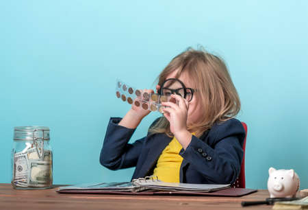 Child numismatist with metal coin in a transparent plastic protection square capsule. Kid with a magnifying glass is considering the old coin numismatist. Financial education. holder caseの写真素材