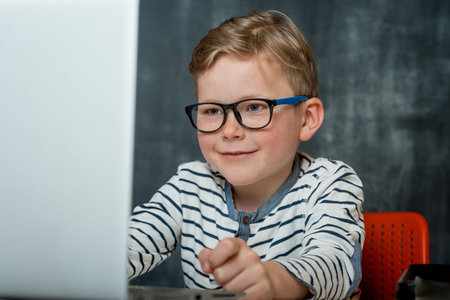 Portrait of excited little kid boy looking at the laptop screen. Child in glasses on the online...
