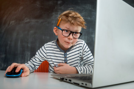 Little kid boy programming with laptop computer. Close up of the portrait of pupil in blue light...
