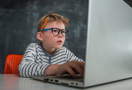 Child boy has online programming lesson. Concentrated kid codding on laptop computer. School at...