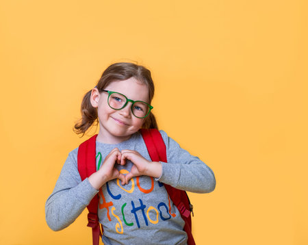 Back to school. Happy kid girl in glasses with backpack showing heart with hands. Friendship...