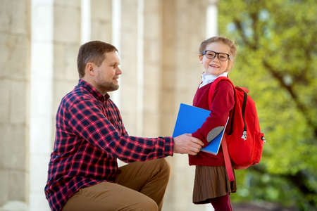 Back to school. First day at school. Father leads little child school girl in first grade. Pupil of primary school with backpack and books in uniform ready for lesson. Portrait of happy smiling kidの写真素材