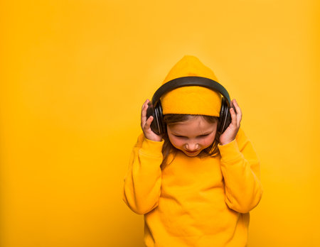 Portrait of stylish cute little kid girl in yellow fashion clothes isolated on yellow color background. Modern child in yellow hat and sweater in headphones listens to the music with copyspace.の写真素材