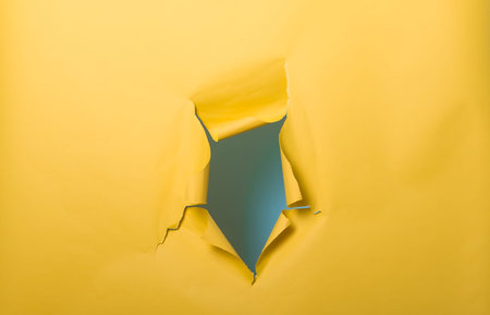 Break through yellow paper wall. Hole with torn sides over yellow background for your text, print or...