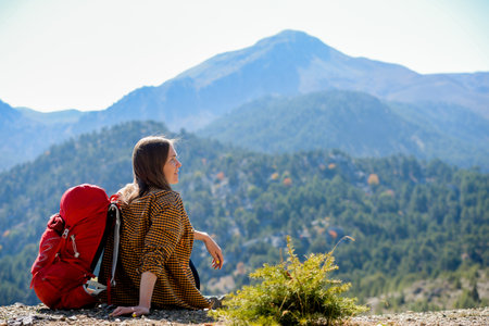 Hiking woman sit on seaside rock. Lady hiker with backpack on top of the mountain and enjoying valley view. Active vacations concept.の写真素材