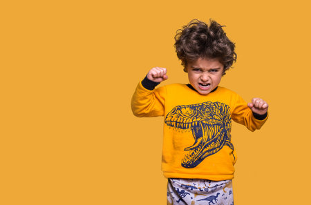 Angry little kid with hands up. Screaming five years old boy is looking at the camera, isolated on yellow background. Shout like a dragon. Hard characterの写真素材
