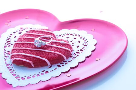 Sugar cookie with engagement ring on pink plate with white doilyの写真素材