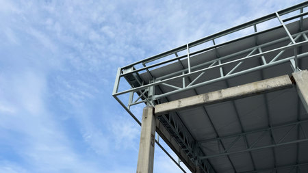 Close-up corner view of a concrete column and steel roof truss structure under construction with...