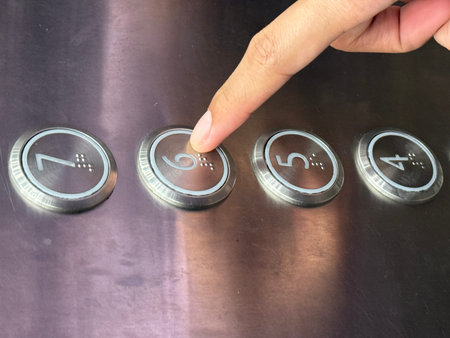 Close-up of a human finger pressing elevator button number six with braille on a stainless steel...