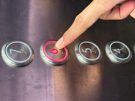 Close-up of a finger pressing an illuminated elevator button number six with braille on a stainless steel panel, representing accessibility, tactile navigation, and modern building design.の写真素材