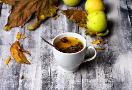 Cup of tea is in the fall on the wooden table, and next are apples and fallen leavesの写真素材