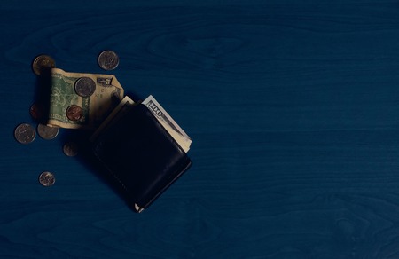 Clip for money with dollar banknotes and some coins scattered around on blue backgroundの写真素材