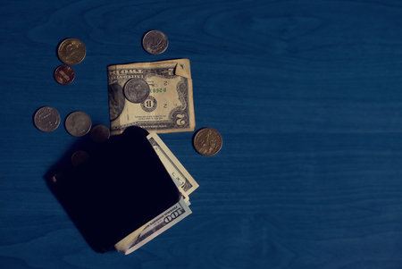 Clip for money with dollar banknotes and some coins scattered around on blue background