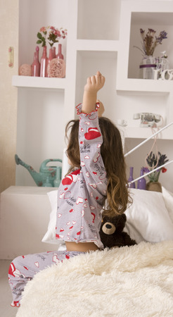 The little girl woke up in a comfortable bedroom and stretches on the bedの写真素材