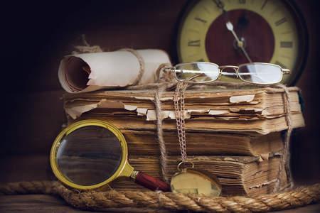 a still life with old scruffy books reading glasses, a clock and a magnifying glass on a dark backgroundの写真素材