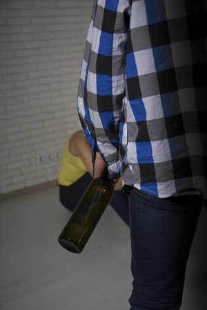 a drunk man in a worn checkered shirt with a bottle of alcohol came home to his distressed wifeの写真素材